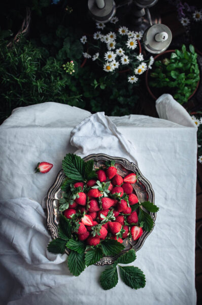 Flatlay photo of strawberries on a silver tray. The tray in on a table covered with white linen.