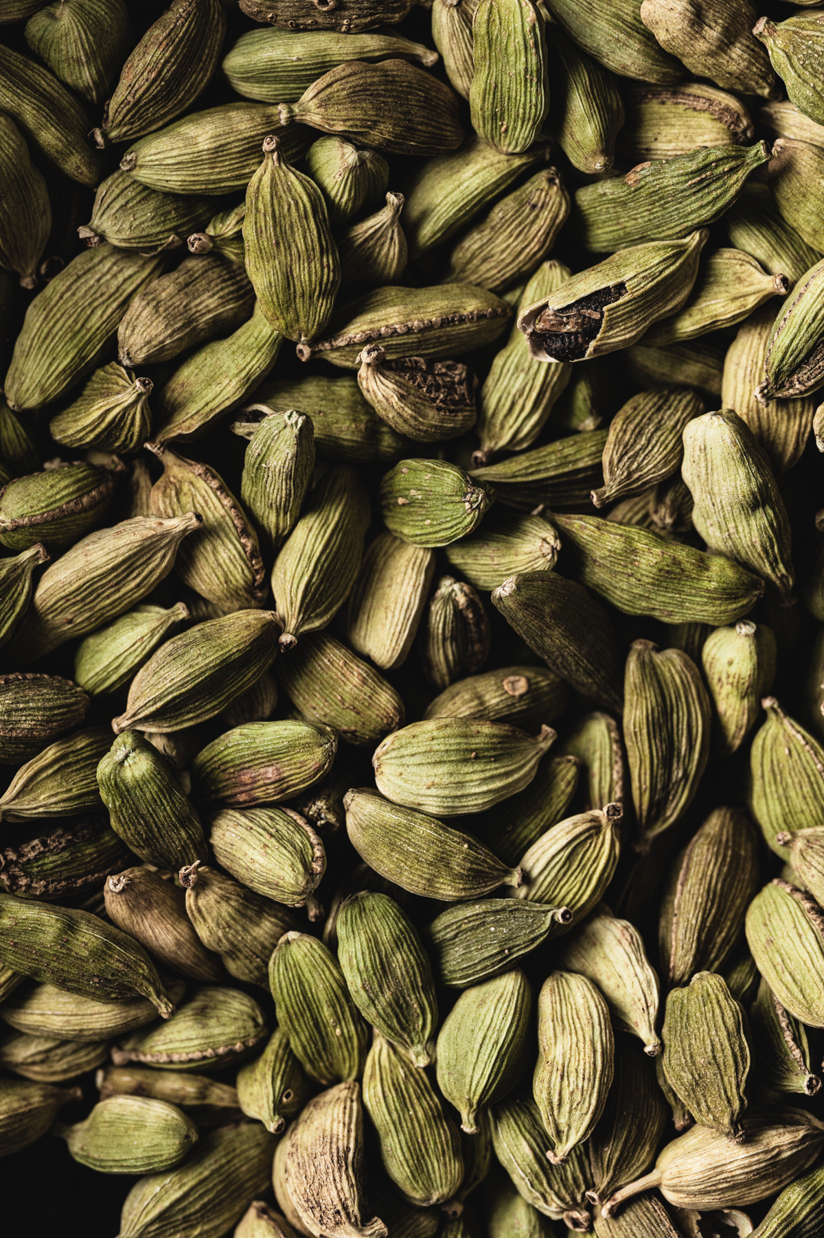 A close up of a lot of whole cardamom pods.