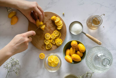 Mini-sized lemon in a bowl and on a cutting board. Two hands in frame slicing the lemons.